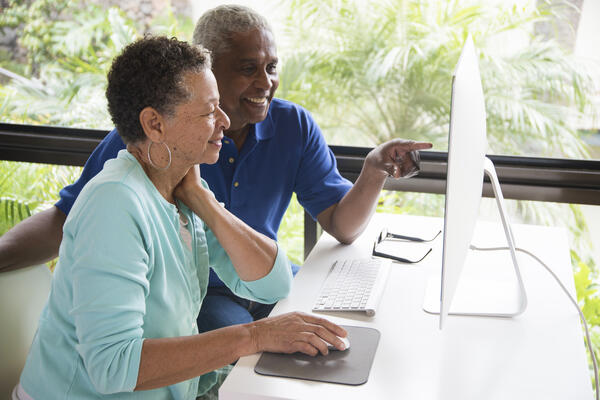 Senior couple sitting at a table viewing a computer screen.